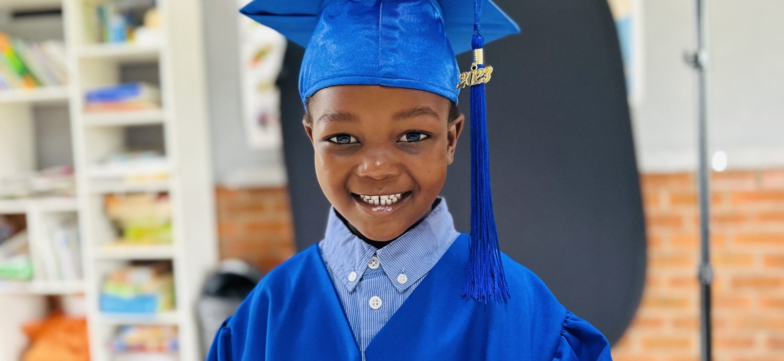 Happy young boy in blue graduation gown and cap smiling at camera.