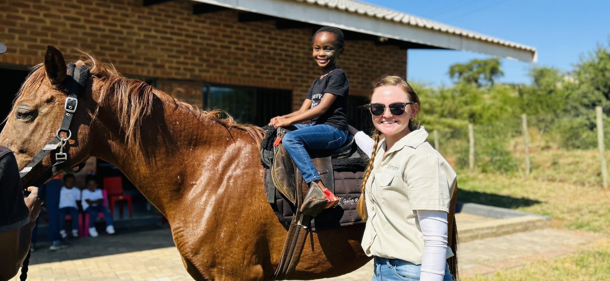Child riding horse with adult supervisor outdoors.