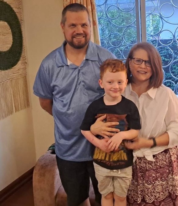 Family of three smiling indoors, with a man, woman, and young boy.