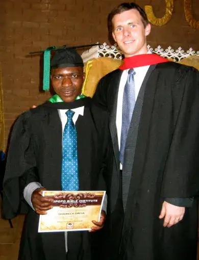 Graduate in academic gown holding diploma at Limpopo Bible Institute.