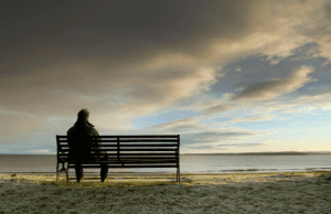 Person sitting alone on a beach bench overlooking the ocean at sunset.