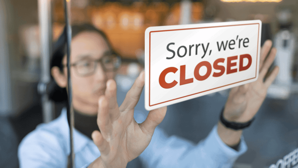 Person placing a 'Sorry, we're CLOSED' sign on a glass door.