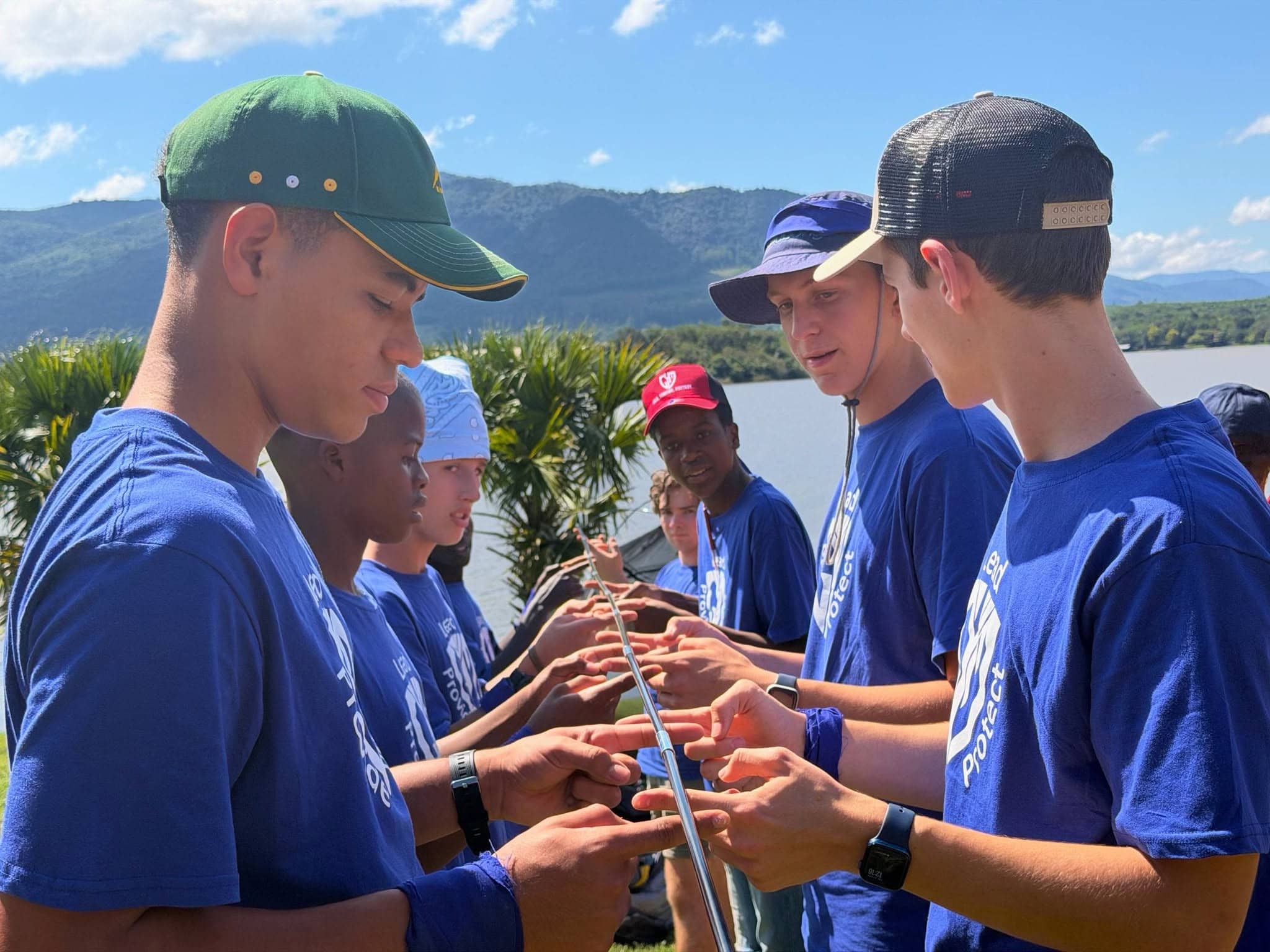 Young men in blue Lead Project shirts participating in a team-building activity outdoors.
